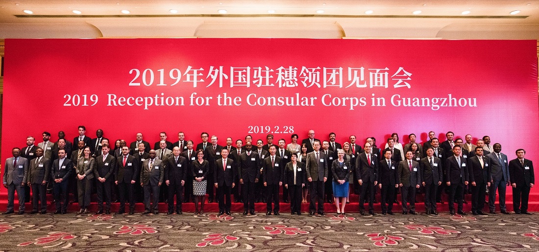 Large group of people in suits, standing in front of a red banner.